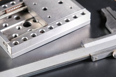 Close up of a precision linear motion guide rail with metal screws and a caliper on a black background.
