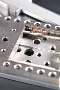 Close up of a precision linear motion guide rail with metal screws and a caliper on a black background.