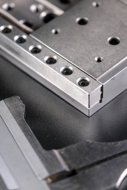 Close up of a precision linear motion guide rail with metal screws and a caliper on a black background.