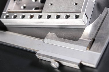 Close up of a precision linear motion guide rail with metal screws and a caliper on a black background.