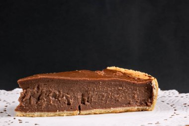 Lezzetli bir dilim çikolatalı tart dantel bir altlığın üzerinde, siyah bir arka planda..