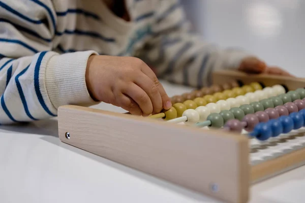 Early development. Little kid toddler sitting at table with educational counting toy, playing with toys made from natural materials, child learning to count numbers in Montessori kindergarten
