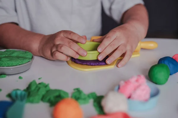 Close up of little kid playing with play dough while sitting at table at home, cropped photo. Sensory indoor activities for toddlers. Creativity and play