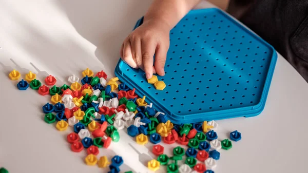 Little child playing peg board mosaic toy at home, sitting at table, inserting colorful pins, developing motor skills. Creative and educational games for toddlers. Sensory activity for small kids