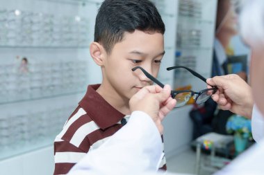 Orta yaşlı göz doktoru genç bir çocuğu muayene ediyor ve Asyalı bir çocuğa göz muayenesi yapıyor.