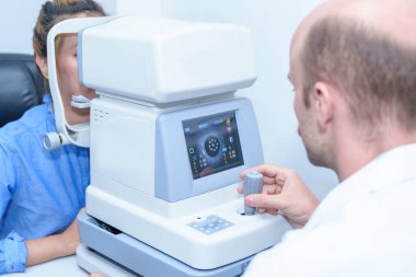 Yakışıklı erkek göz doktoru modern bir klinikte çekici bir genç kadının vizyonunu inceliyor, göz doktorları ve hastalar.