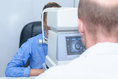 Yakışıklı erkek göz doktoru modern bir klinikte çekici bir genç kadının vizyonunu inceliyor, göz doktorları ve hastalar.