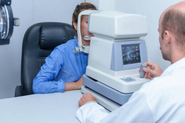 Yakışıklı erkek göz doktoru modern bir klinikte çekici bir genç kadının vizyonunu inceliyor, göz doktorları ve hastalar.