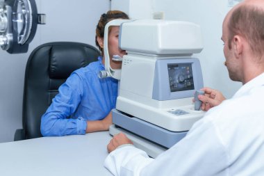 Yakışıklı erkek göz doktoru modern bir klinikte çekici bir genç kadının vizyonunu inceliyor, göz doktorları ve hastalar.
