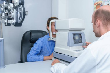 Yakışıklı erkek göz doktoru modern bir klinikte çekici bir genç kadının vizyonunu inceliyor, göz doktorları ve hastalar.
