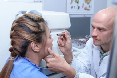 Doktor göz doktoru hastanın gözlerini muayene eder..