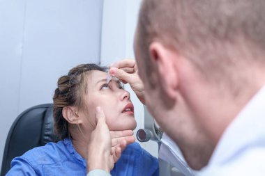 Erkek doktor göz doktorları göz hekimliği muayenehanesinde tedavi sırasında bir kadın hastanın gözlerine damla damlatıyor.