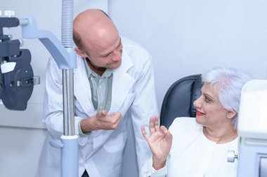 Çekici erkek göz doktoru, modern klinikte, doktorlarda ve göz hekimliği kliniğinde orta yaşlı bir kadının görme duyusunu kontrol ediyor..