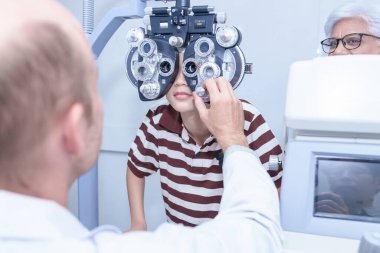 Göz muayenesi sırasında optik fosforopterden bakan Asyalı çocuk, teşhis göz hekimi ekipmanları, seçici odaklanma