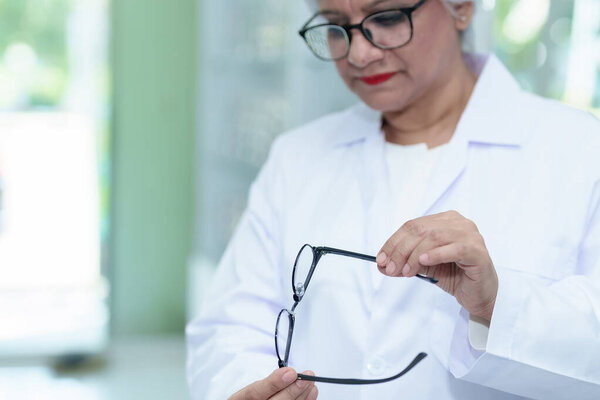  Middle aged ophthalmologist holding eyeglasses and examining them, focus on eyeglasses, close-up