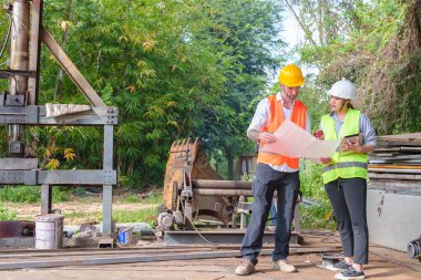 Hard Hats 'deki erkek ve kadın endüstriyel mühendisler dizüstü bilgisayar kullanırken yeni projeleri tartışıyorlar. Ağır bir endüstriyel fabrikada çalışırken jestler yapıyorlar..