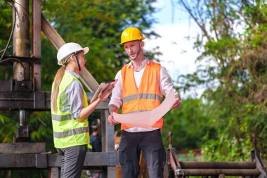 Hard Hats 'deki erkek ve kadın endüstriyel mühendisler dizüstü bilgisayar kullanırken yeni projeleri tartışıyorlar. Ağır bir endüstriyel fabrikada çalışırken jestler yapıyorlar..