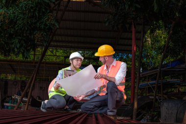 Hard Hats 'deki erkek ve kadın endüstriyel mühendisler dizüstü bilgisayar kullanırken yeni projeleri tartışıyorlar. Ağır bir endüstriyel fabrikada çalışırken jestler yapıyorlar..