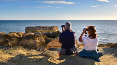 Dürbünlü bir çift kayalıklardaki deniz kuşlarını izliyor, Algarve sahilleri, Portekiz, Avrupa