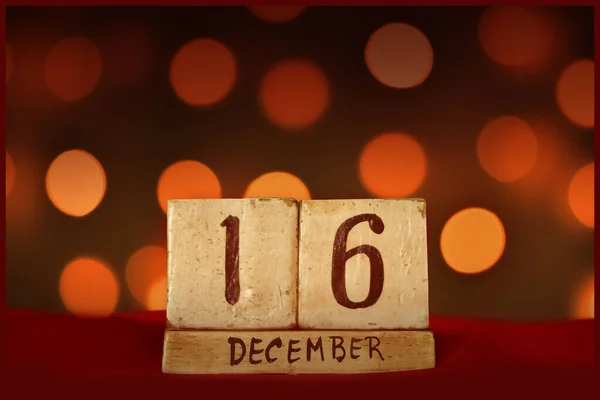 16 Aralık 'ta kırmızı kumaş üzerine ahşap blok takvimi, şenlikli Bokeh ışıkları arka plan tebrik kartı bayramları, doğum günleri, özel günler için tarih kaydet..