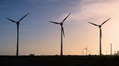 Rüzgar türbinleri elektrik üretir, gün batımında yel değirmeni siluetleri.