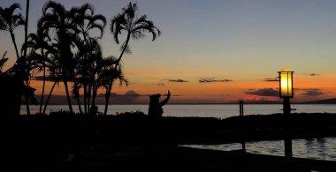 Hawaii hula dansçısının silueti gün batımında okyanus kenarında, plajda palmiye ağaçları eşliğinde, Lahaina, Maui, Hawaii