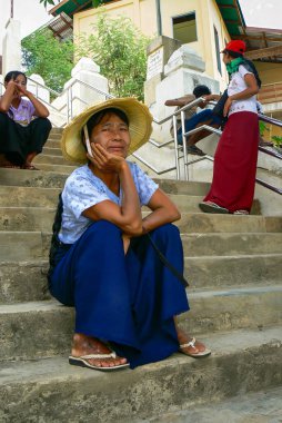 Bagan, Myanmar - 16 Temmuz 2008: Güneş koruması için hasır şapka giyen Burmalı kadın merdivenlerde oturmuş kameraya bakıyor, Myanmar, Burma, Asya