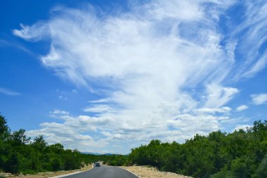 Kümülüs ve sirrus bulutları mavi gökyüzünde yol boyunca yükseliyor, araba caddede. Karadağ gezisi, Balkanlar gezisi, Karadağ seyahati