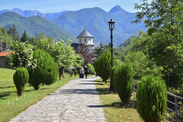 stock image Kolasin, Montenegro - June 7, 2024: Elderly couple walking on footpath at picturesque serbian orthodox Moraca Monastery. Popular tourist destination.