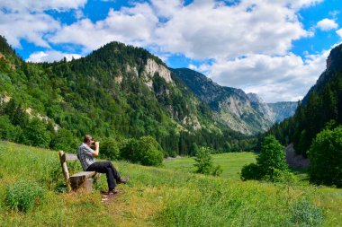 Tourist on bench taking photograph of amazing Susicko lake green valley, dry in summer. Natural beauty in Durmitor National  Park Montenegro,  explore the Balkans, travel Europe. clipart