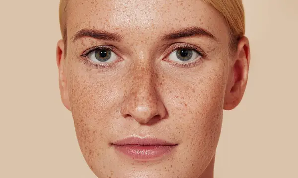 Çilli genç bir kadının yakın çekim stüdyo fotoğrafı. Doğal güzelliğin portresi, pürüzsüz tenli, pastel arka planda..