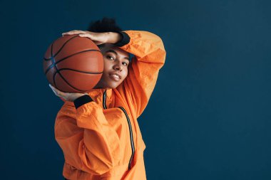 Genç bir basketbolcunun portresi topla mavi zemine karşı duruyor ve kameraya bakıyor.