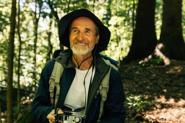 Sırt çantalı ve kameralı neşeli son sınıf öğrencisi bir orman yürüyüşü sırasında mola veriyor.