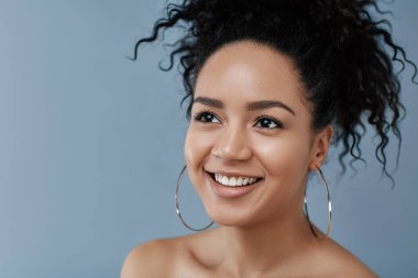 Siyah kıvırcık saçlı, gülümseyen bir kadının kesilmiş stüdyo portresi.