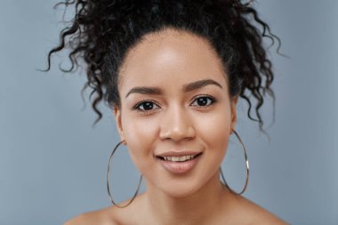 Güzel bir bayanın, mavi bir arka fonun üzerinden, küpe takarak kameraya bakışını kapatın.