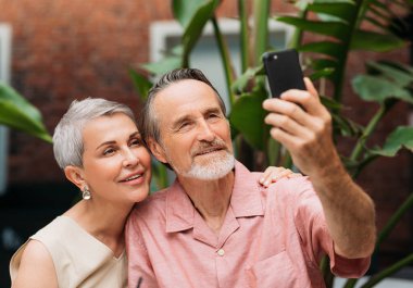 Gülümseyen son sınıf öğrencileri dışarıda otururken akıllı telefondan selfie çekiyorlar.