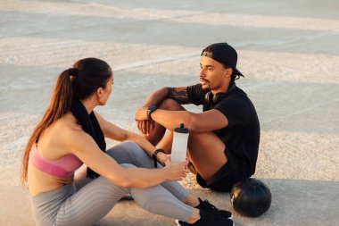 Spor yaparken, gün batımında çatıda birlikte oturan spor yapan çift.