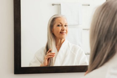 Yaşlı kadın, banyo aynasındaki uzun gri saçlarına hayran.