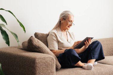 Dijital tablet kullanarak koltukta oturan yaşlı bir kadın. 