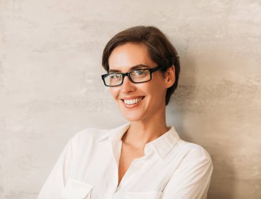 Gözlüklü neşeli beyaz girişimci duvara yaslanıp kameraya bakıyor.