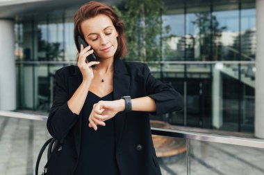 Orta yaşlı bir iş kadını cep telefonuyla konuşurken akıllı bakışlarına bakıyor.