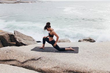 Paspasın üzerindeki kadın vücudunu ısıtıyor. Kadın sporcu okyanus kenarında esneklik egzersizleri yapıyor..