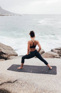 Akşamları sıska bir kadının okyanus kenarında yoga yapışının arka görüntüsü.