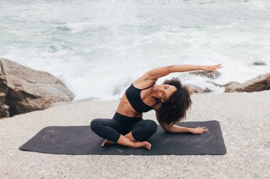 Okyanus kenarında antrenman yapmadan önce vücudunu ısıtan bir kadın. 