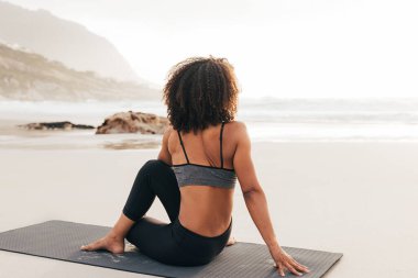 Gün batımında plajda bir paspasda oturan kadın. Yoga egzersizlerinden sonra dinlenen bir kadının arka planı..
