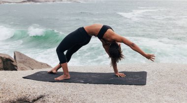 Okyanusun kıyısındaki minderde yoga yapan zayıf kadının yan görüntüsü.