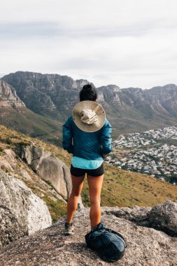 Rear view of young female standing on a mountain top and looking at view clipart