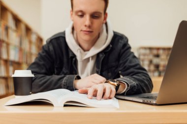 Erkek elini bir kitabın üzerine koy. Üniversite öğrencisi kütüphanede otururken kitaptan okuyor.