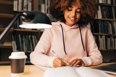 Kıvırcık saçlı güzel öğrenci, akşam kütüphanede ders çalışıyor.