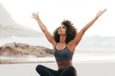 Gün batımında sahilde otururken Urdhva Hastasana yoga pozu veren genç bir kadın.